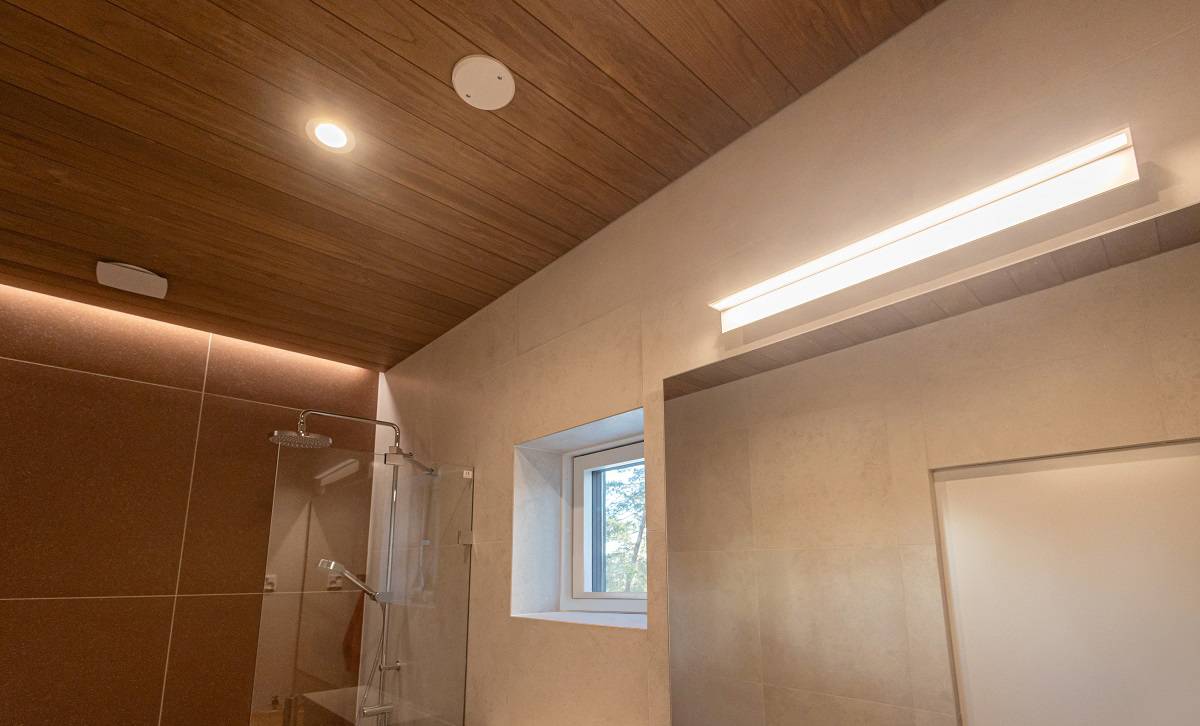 L'éclairage de la salle d'eau se compose d'une applique murale BLADE600 sur le miroir, de downlights au plafond et d'une bande LED à éclairage indirect dans la rainure du plafond sur le mur principal près de la douche.